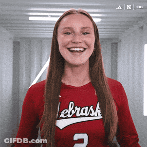 A Woman Wearing A Red Lebrask Jersey Smiles For The Camera GIF