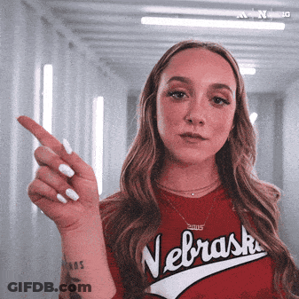 A Woman Wearing A Red Nebraska Shirt Is Pointing At Something GIF