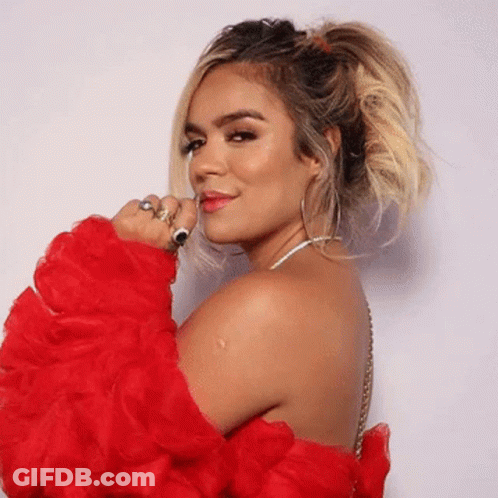 A Woman Wearing A Red Ruffled Sleeved Top Is Looking Over Her Shoulder At The Camera GIF