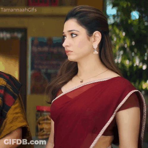A Woman Wearing A Red Saree And Earrings Stands In Front Of A Sign That Says " Tamannahgifs " GIF