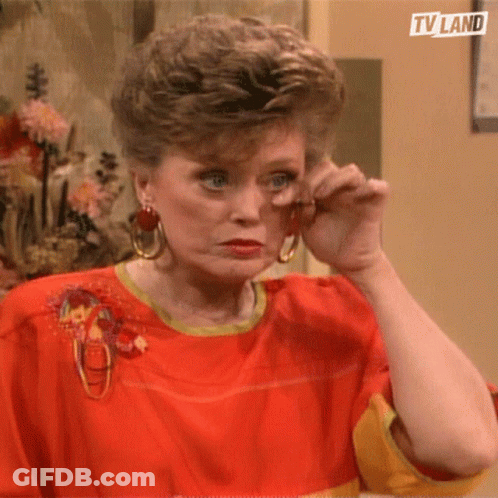 A Woman Wearing A Red Shirt And Earrings Wipes Her Eyes With Her Hand .. GIF