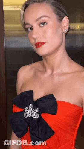 A Woman Wearing A Red Strapless Dress With A Black Bow On It GIF