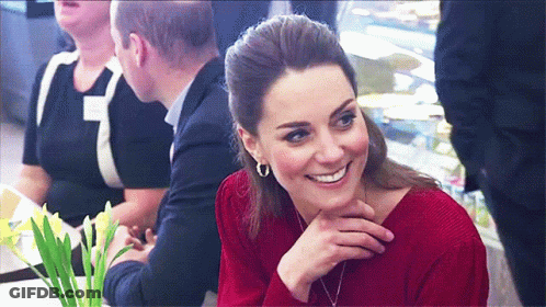 A Woman Wearing A Red Sweater Is Smiling While Sitting At A Table GIF