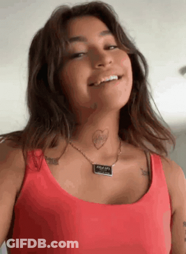 A Woman Wearing A Red Tank Top And A Necklace Has A Tattoo Of A Heart On Her Neck . GIF