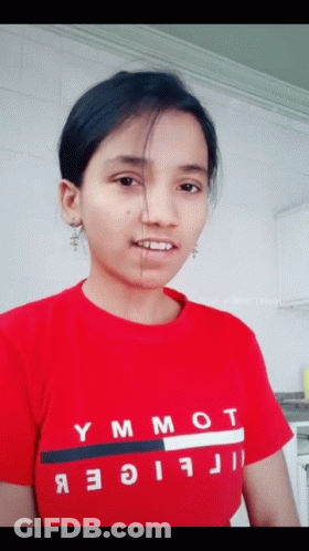 A Woman Wearing A Red Tommy Hilfiger Shirt Looks At The Camera GIF