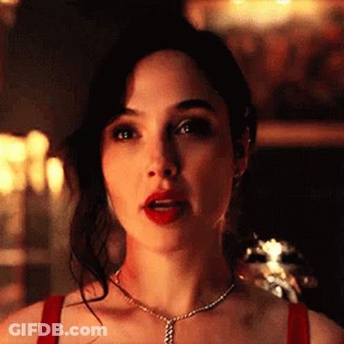 A Woman Wearing A Red Top And A Necklace Is Looking At The Camera . GIF