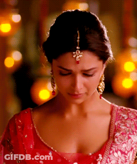 A Woman Wearing A Red Top And Gold Earrings Looks Down At Something GIF