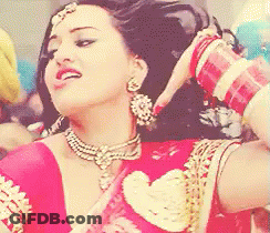 A Woman Wearing A Red Top And Gold Jewelry Is Smiling GIF