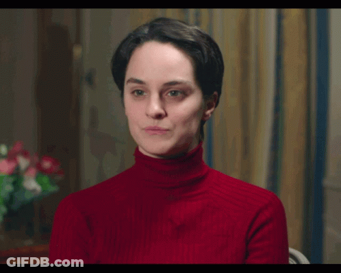 A Woman Wearing A Red Turtleneck Sweater Is Sitting In A Chair GIF