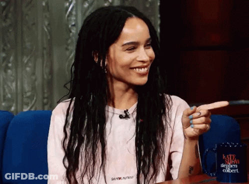 A Woman Wearing A Saint Laurent Shirt Is Smiling And Pointing At Something GIF