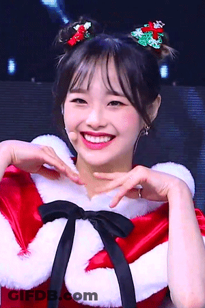 A Woman Wearing A Santa Costume Is Smiling And Making A Heart Shape With Her Hands GIF