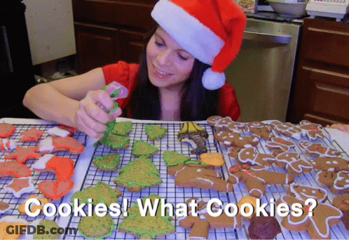 A Woman Wearing A Santa Hat Decorates Gingerbread Cookies With The Words Cookies What Cookies Below Her GIF