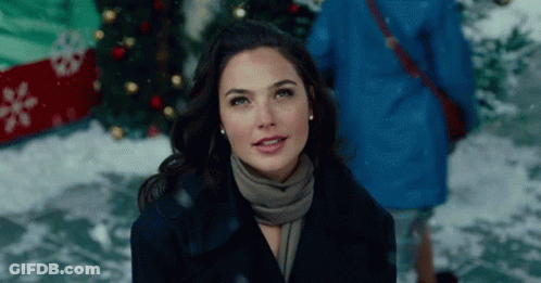 A Woman Wearing A Scarf And A Coat Is Standing In Front Of A Christmas Tree . GIF