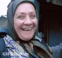 A Woman Wearing A Scarf And A Head Scarf Is Smiling For The Camera . GIF