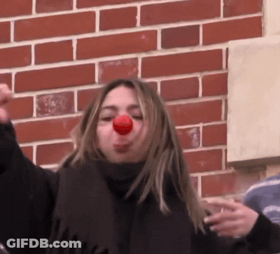 Woman With Scarf And Red Nose In Front Of Brick Wall GIF