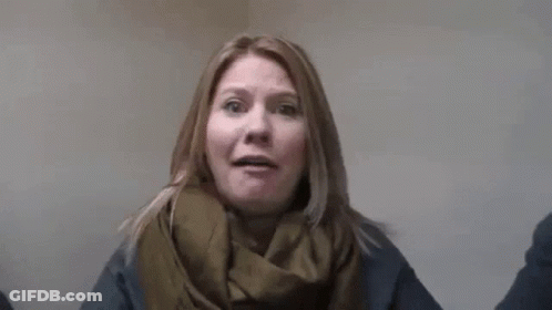 A Woman Wearing A Scarf And A Sweater Is Standing In Front Of A Wall With Her Arms Outstretched . GIF