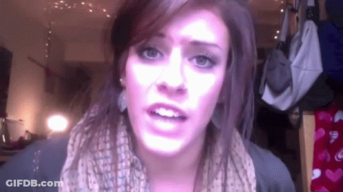 A Woman Wearing A Scarf And Earrings Looks At The Camera GIF