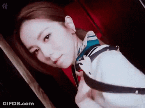 A Woman Wearing A Scarf Around Her Neck Is Taking A Selfie In A Dark Room . GIF