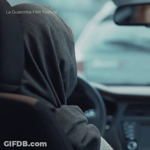A Woman Wearing A Scarf Is Driving A Car With La Guarimba Film Festival Written On The Bottom Of The Image GIF