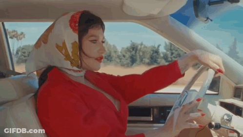 A Woman Wearing A Scarf Is Driving A Car . GIF