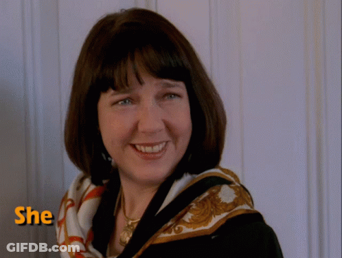 A Woman Wearing A Scarf Smiles In Front Of A Wall With The Word She Above Her GIF