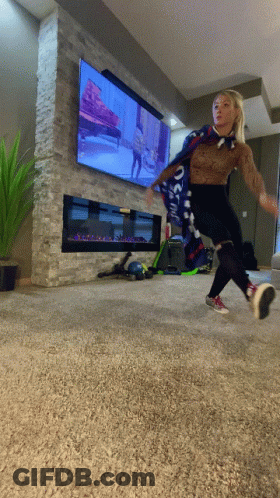A Woman Wearing A Scarf That Says ' Oakland ' On It Is Jumping In Front Of A Television GIF