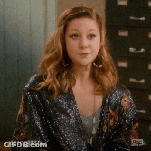 A Woman Wearing A Sequined Jacket And Hoop Earrings Is Sitting In Front Of A Filing Cabinet . GIF
