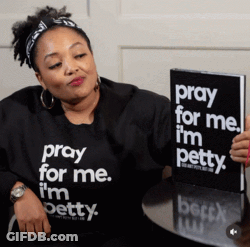 A Woman Wearing A Shirt That Says Pray For Me I 'M Petty Is Holding A Book GIF