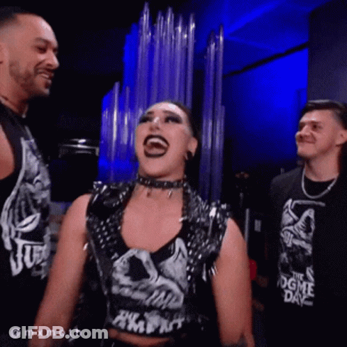 A Woman Wearing A Shirt That Says ' The Dogme Day ' Is Laughing With Two Men GIF