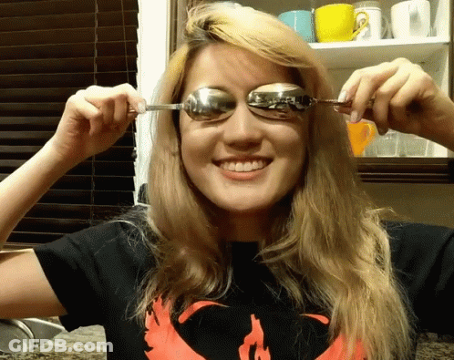 A Woman Wearing A Shirt With A Phoenix On It Is Holding A Spoon To Her Eye GIF
