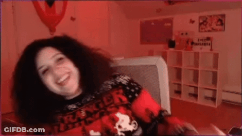 A Woman Wearing A Stranger Things Sweater Is Sitting On A Couch . GIF