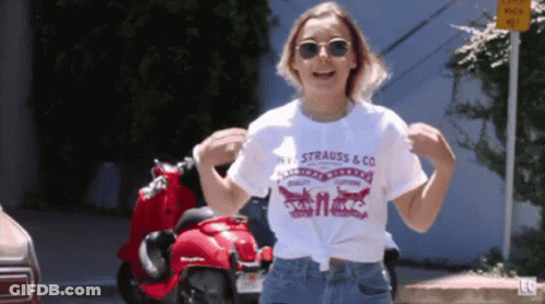 A Woman Wearing A Strauss & Co T-Shirt Is Dancing In Front Of A Red Scooter GIF