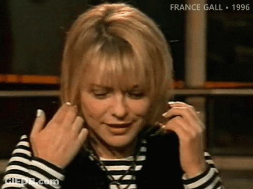 A Woman Wearing A Striped Shirt And A Black Vest Adjusts Her Hair GIF