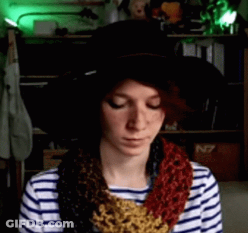 A Woman Wearing A Striped Shirt And A Hat With A Scarf Around Her Neck Is Looking Down GIF