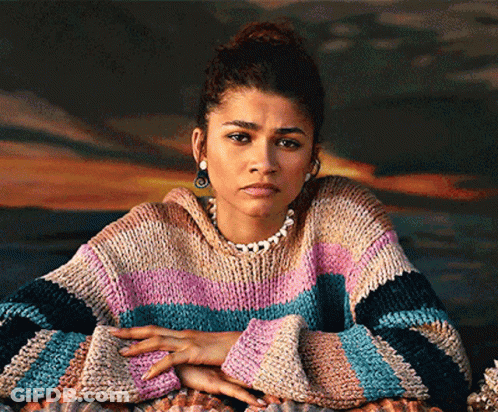 A Woman Wearing A Striped Sweater And A Pearl Necklace Looks At The Camera GIF