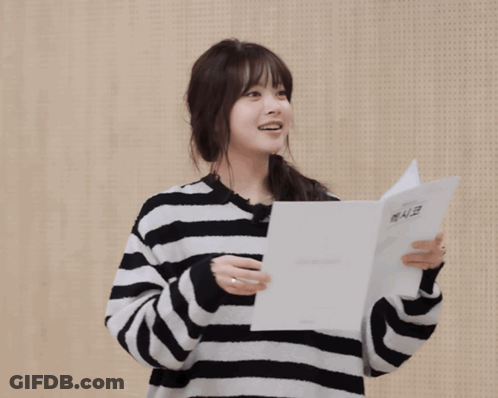 A Woman Wearing A Striped Sweater Holds A Piece Of Paper And Says Gracias In A Foreign Language GIF