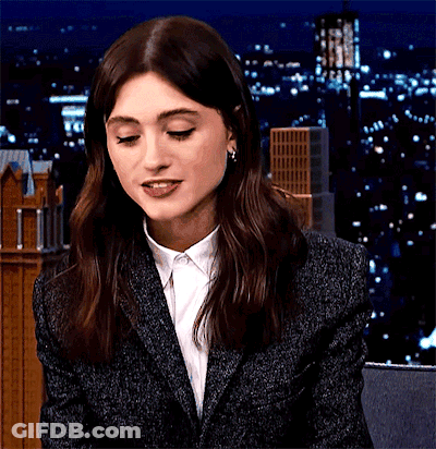 A Woman Wearing A Suit And A White Shirt Is Smiling At The Camera . GIF