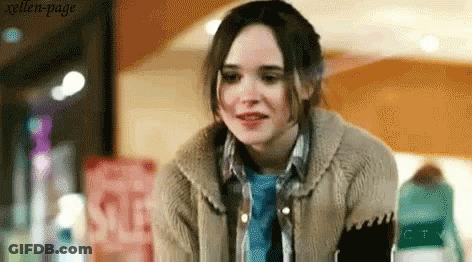 A Woman Wearing A Sweater And A Blue Shirt Is Standing In Front Of A Sign That Says Sale . GIF