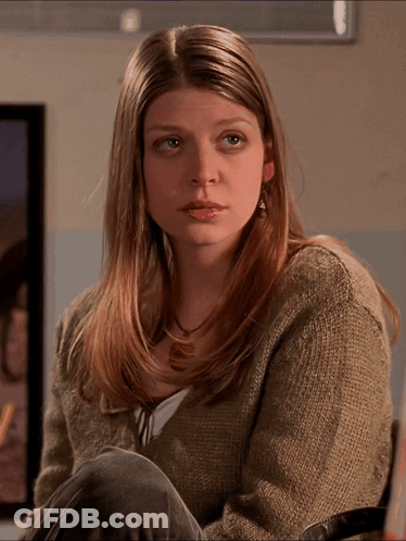 Woman In Sweater And Earrings Sitting In Front Of Framed Picture GIF