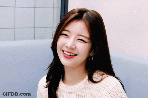 A Woman Wearing A Sweater And Hoop Earrings Smiles For The Camera GIF