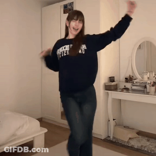 A Woman Wearing A Sweater That Says " Abercrombie & Fitch " Is Dancing In A Bedroom GIF