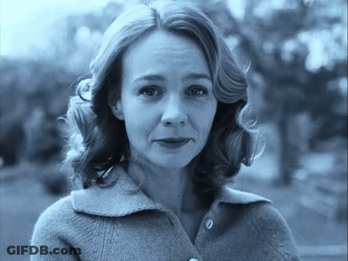 A Woman Wearing A Sweater With Buttons On The Front Looks At The Camera GIF