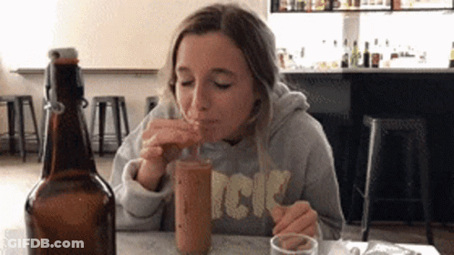 A Woman Wearing A Sweatshirt That Says Acdc Drinks From A Bottle GIF