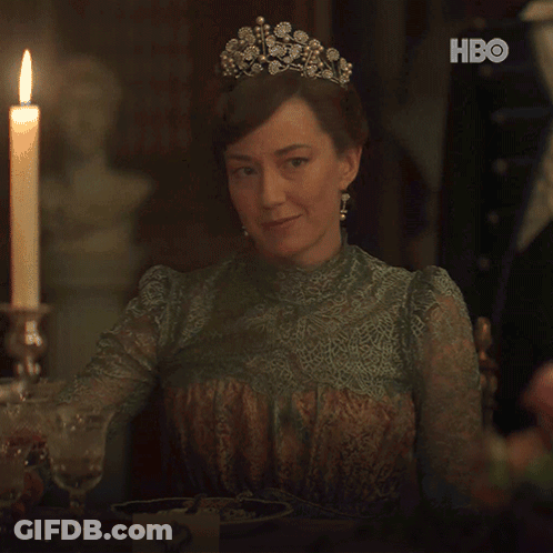 A Woman Wearing A Tiara Is Holding A Glass Of Wine In Front Of A Candle And Hbo Logo GIF