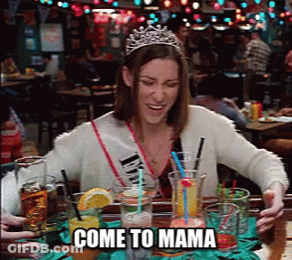 A Woman Wearing A Tiara Is Sitting At A Table With Drinks And The Words Come To Mama Below Her GIF