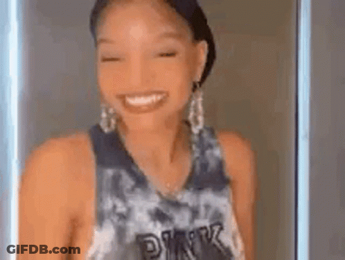 A Woman Wearing A Tie Dye Tank Top And Earrings Is Smiling . GIF