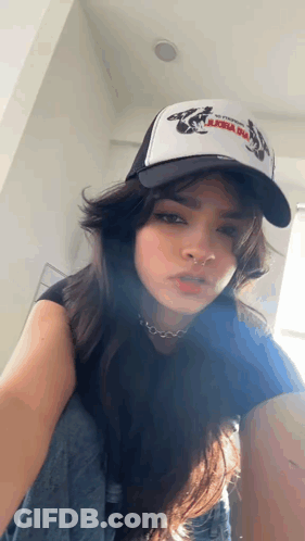 A Woman Wearing A Trucker Hat And A Nose Ring Is Kneeling Down . GIF