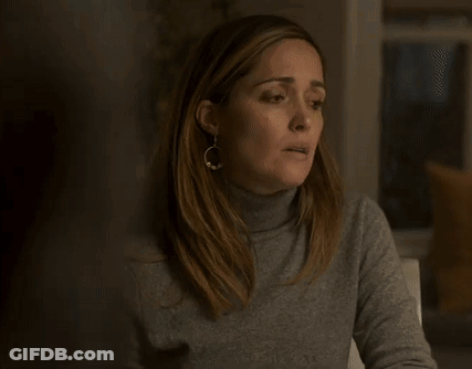 A Woman Wearing A Turtleneck Sweater And Earrings Is Sitting At A Table With Her Mouth Open . GIF