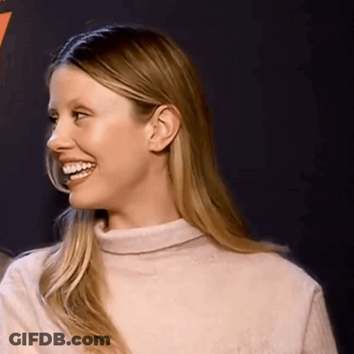 A Woman Wearing A Turtleneck Sweater Is Smiling And Looking To The Side . GIF