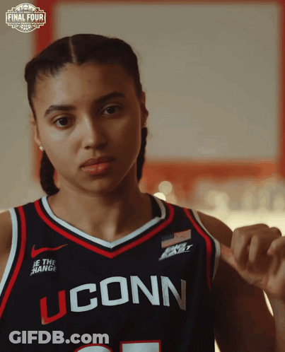 A Woman Wearing A Uconn Basketball Jersey Looks At The Camera GIF